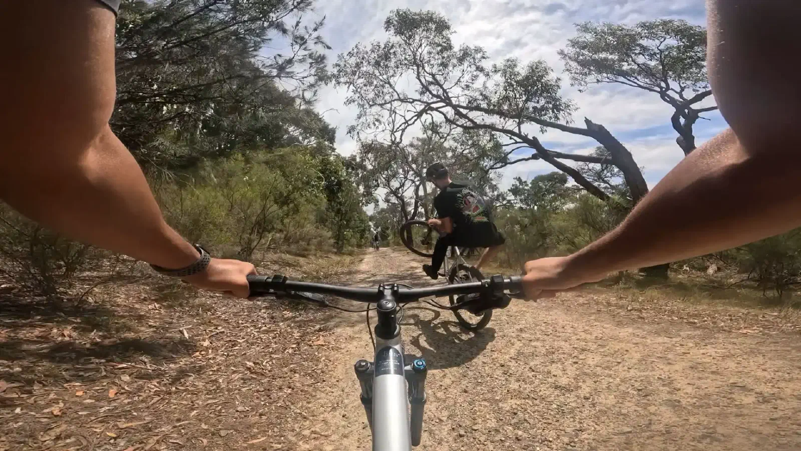 A riderâs view over mountain bike handlebars of a bush trail, following another rider