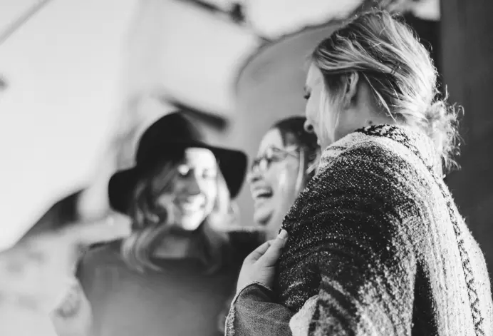 A grayscale shot of three women smiling and laughing.